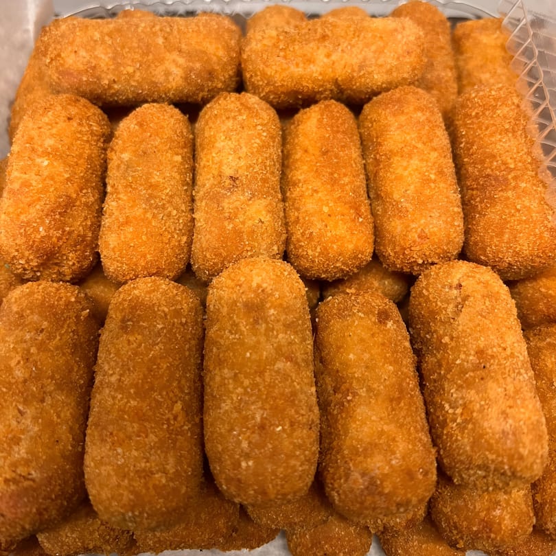 Close-up of many golden-brown Cuban croquettes, breaded and fried, in a clear plastic container.