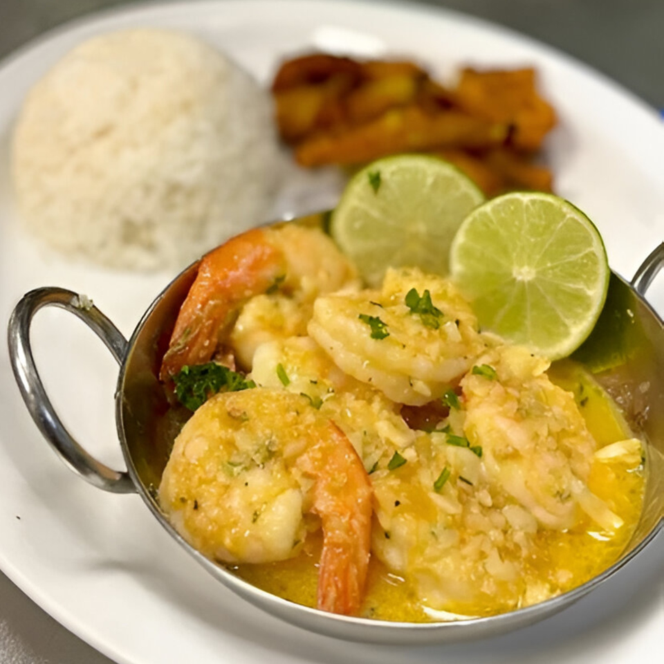 Garlic shrimp in a metal bowl with lime slices, rice, and plantains on a white plate.