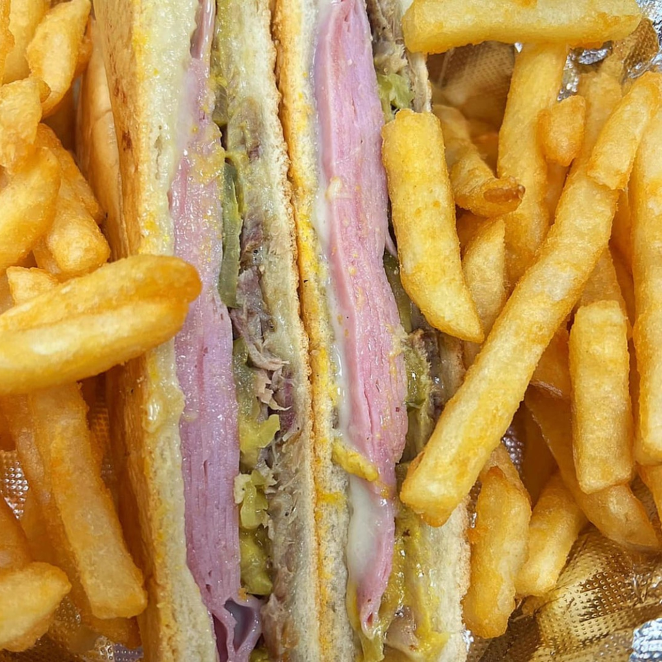 Close-up of a Cuban sandwich with ham, cheese, and pickles, served with golden french fries.