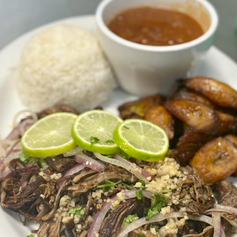 Cuban shredded beef with lime, red onions, rice, plantains, and a side of sauce.