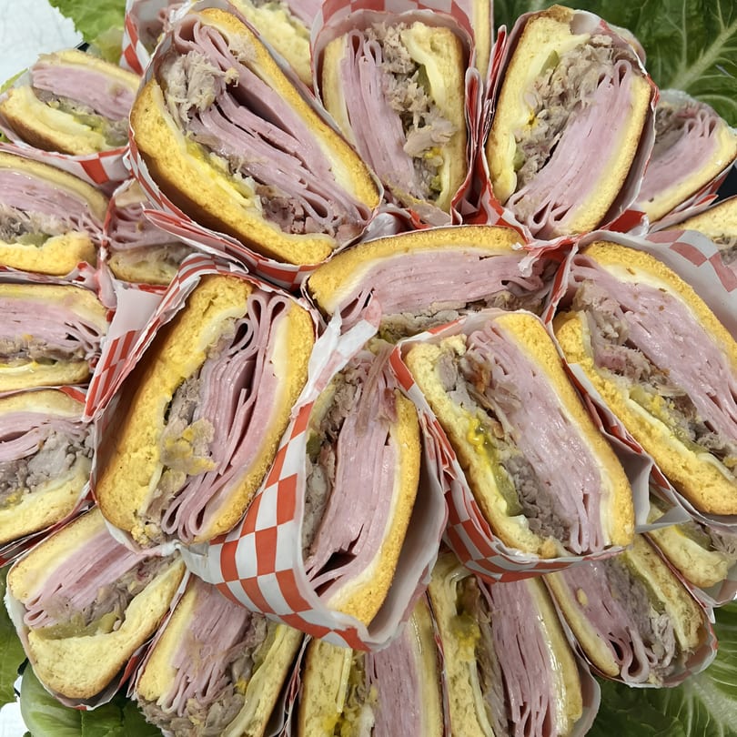 Close-up of many Cuban sandwiches, cut in half, wrapped in red and white checkered paper.